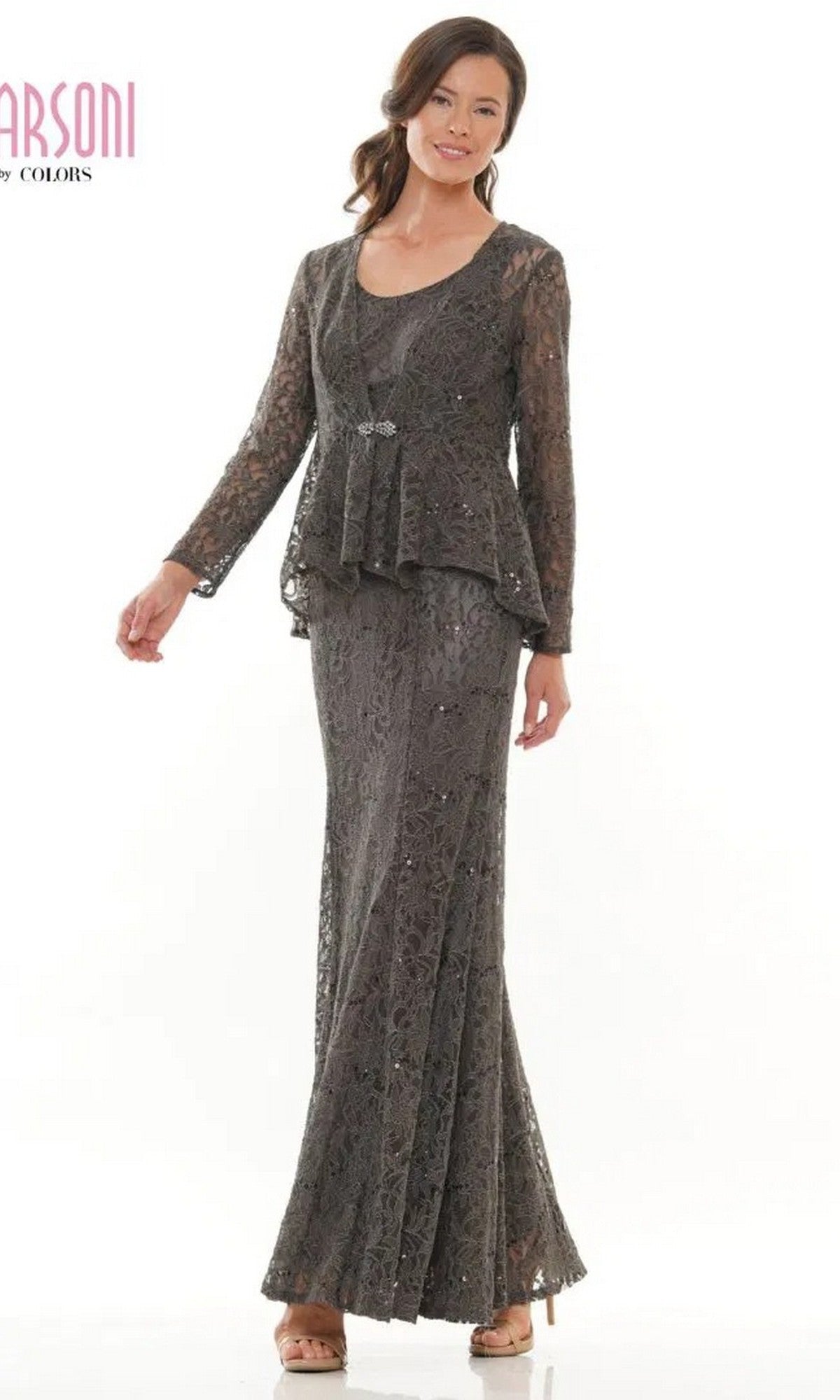 A woman stands against a white background wearing the Marsoni M301 long formal dress in charcoal, featuring lace detailing, a peplum waist, and a decorative brooch.